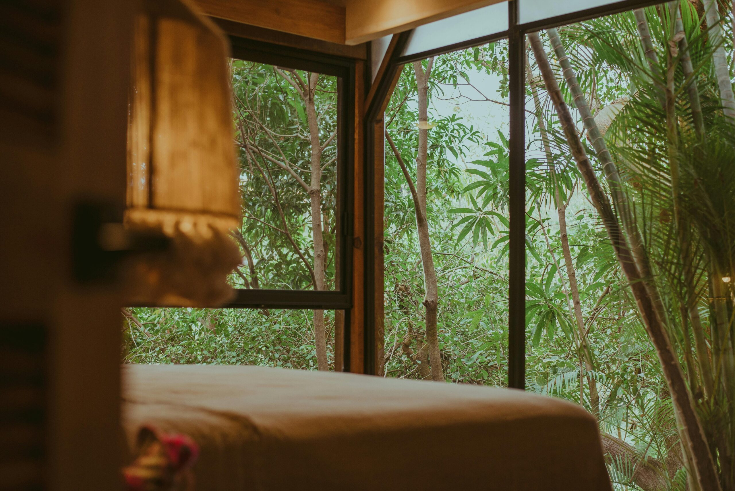 Cozy bed in a luxurious resort overlooking a lush tropical forest through large windows.