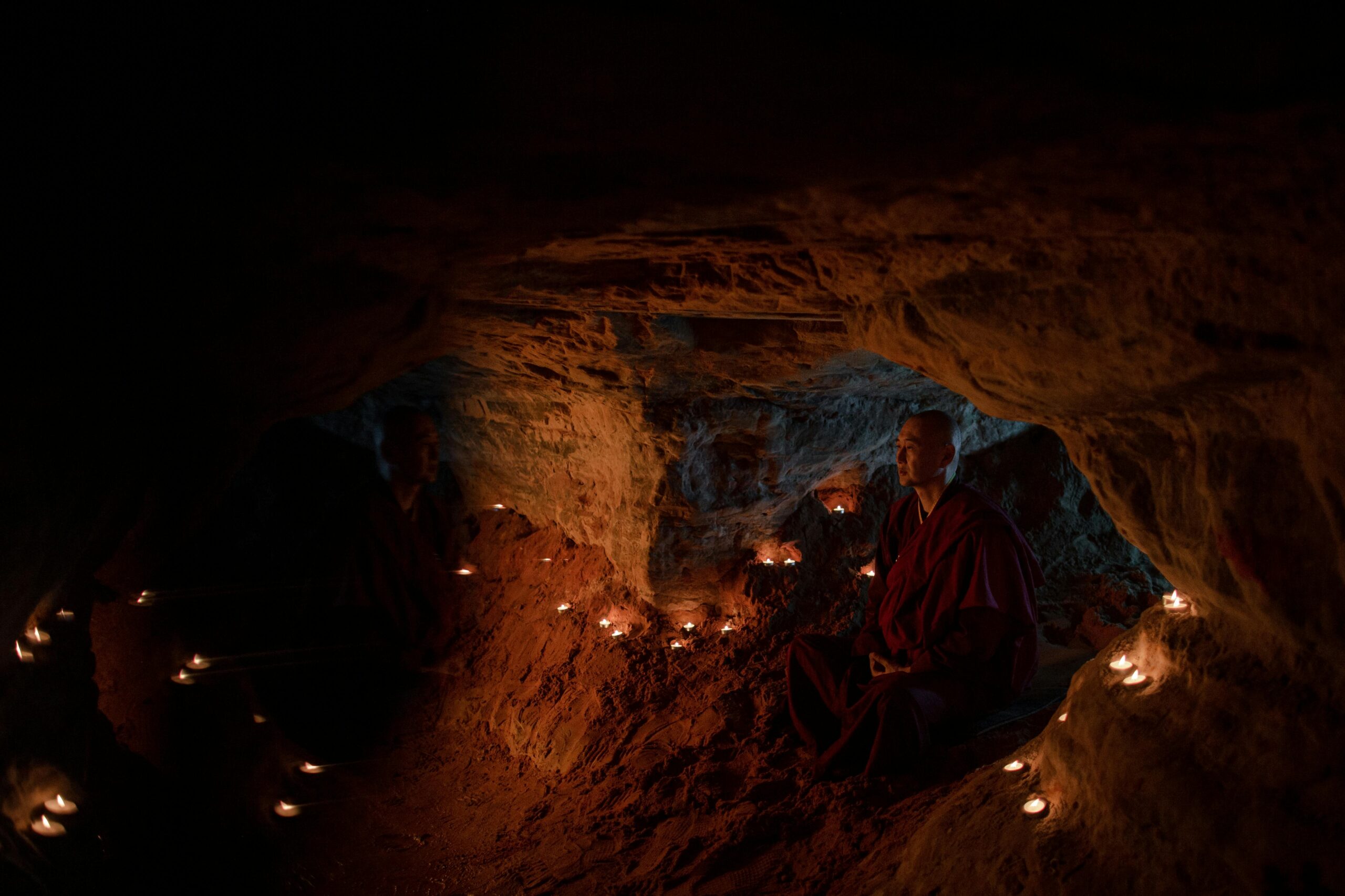 A monk meditates peacefully in a serene, candlelit cave, creating a tranquil religious atmosphere.